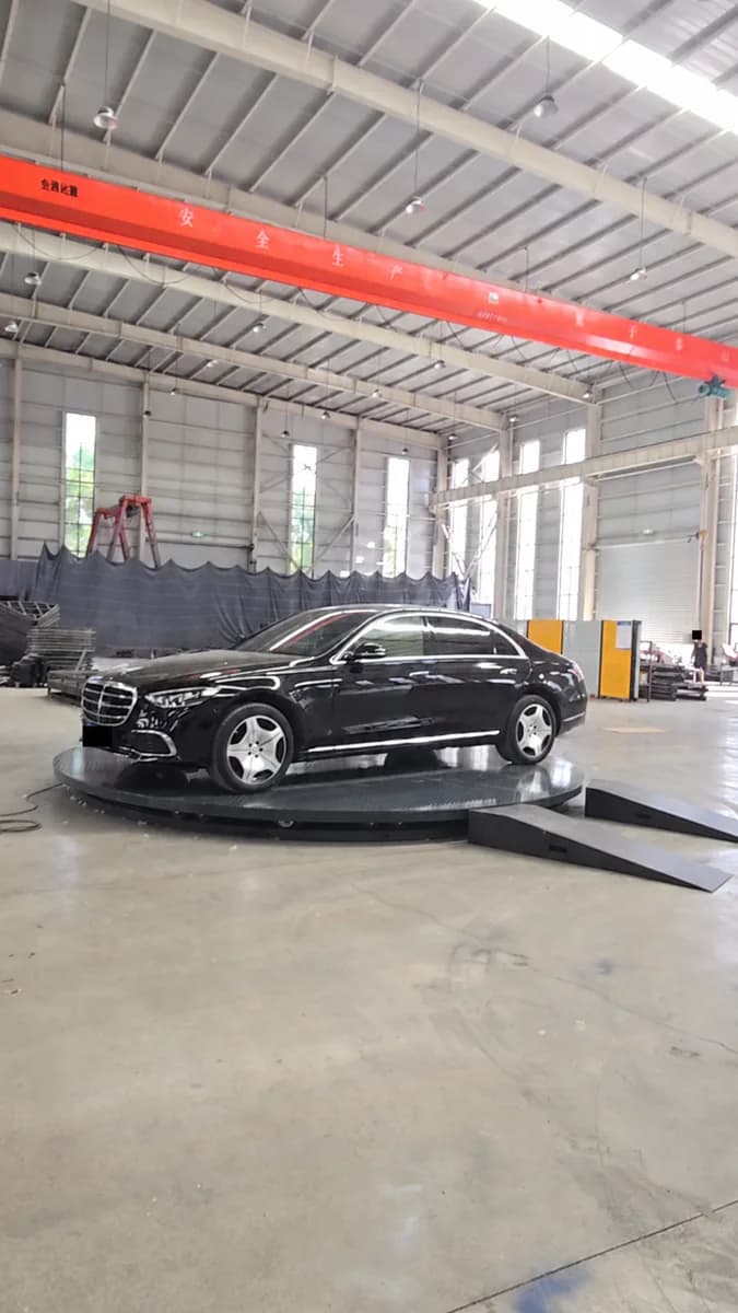 Car on a black circular turntable with approach ramps in a workshop